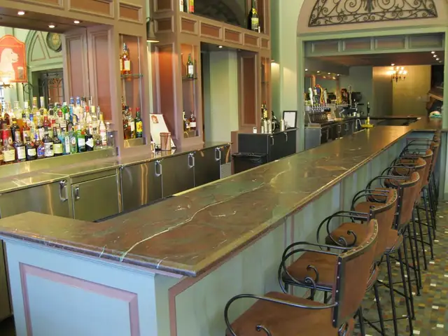 Long stone-topped bar with a raised rail, wood back bar and bar stools